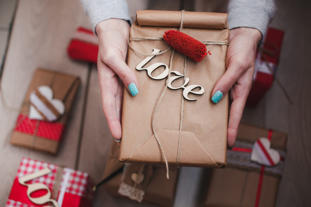 Handen houden een met touw verpakt feelgood-cadeau vast met het woord 'love' en een rode decoratie.