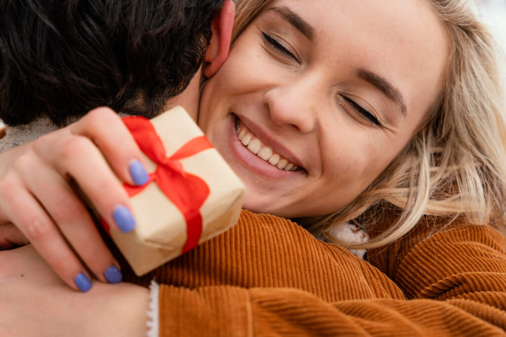 Vrouw omhelst iemand blij met een klein feelgood-cadeau met rood lint in haar hand.